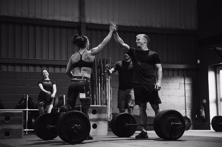 Athletes high-fiving over barbells after a workout